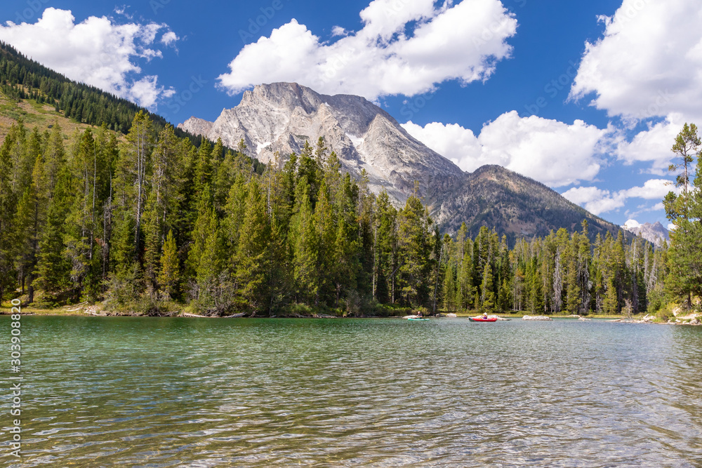 People relaxing on boats on a lake in Teton National Park. It is surrounded by trees and mountains