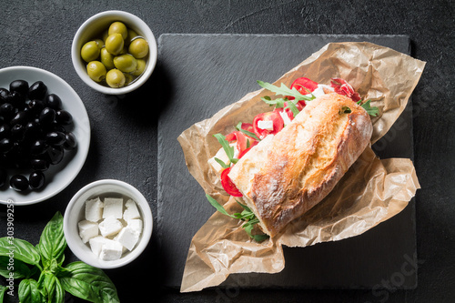 Sandwich with jamon, cheese, tomatoes and arugula on a black background