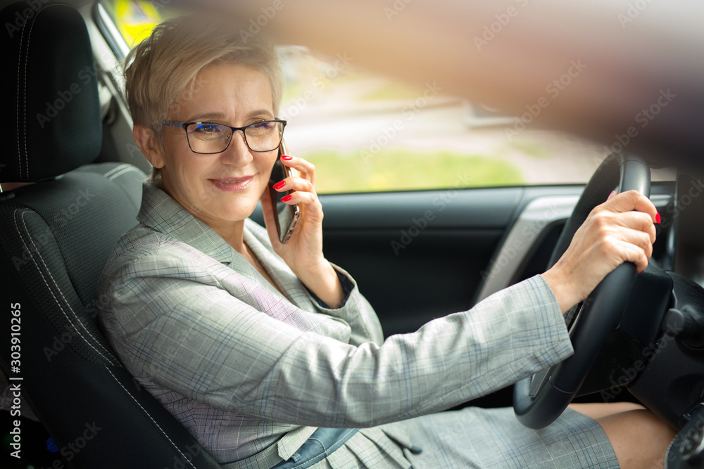 Φωτογραφία adult woman in a suit with a phone in his hand in a car driving