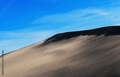 Sand dune with dark shadow on blue sky background