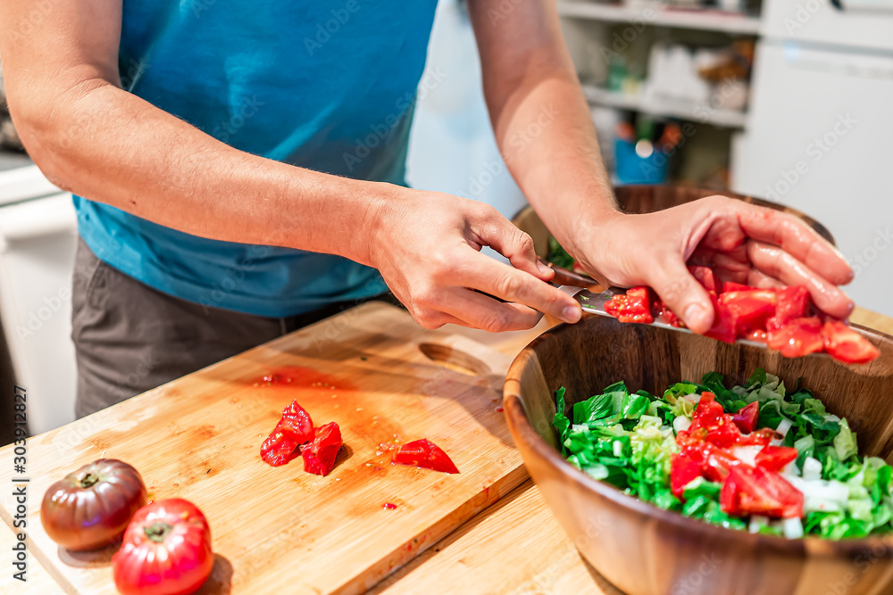Man chopping vegetables on cutting board table in kitchen placing juicy red heirloom tomatoes with vibrant color from garden into salad wooden bowl