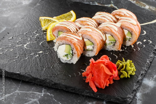 Sushi Rolls with flamed salmon, cucumber and Cream Cheese inside on black slate isolated on black marble background. Philadelphia roll sushi with cucumber. Sushi menu. Horizontal photo.