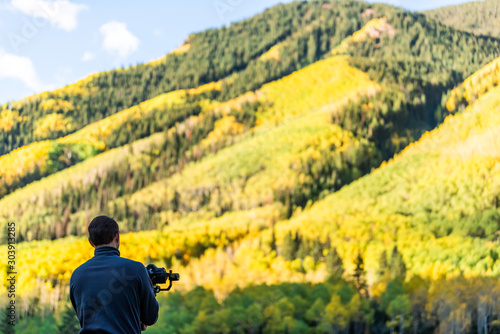 Castle Creek road view with man holding camera gimbal filming colorful yellow leaves foliage on aspen trees in Colorado rocky mountains autumn fall