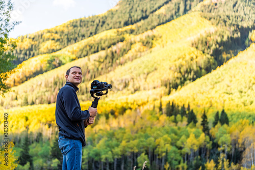 Castle Creek road view with happy man holding camera gimbal filming colorful yellow leaves foliage on aspen trees in Colorado rocky mountains autumn fall