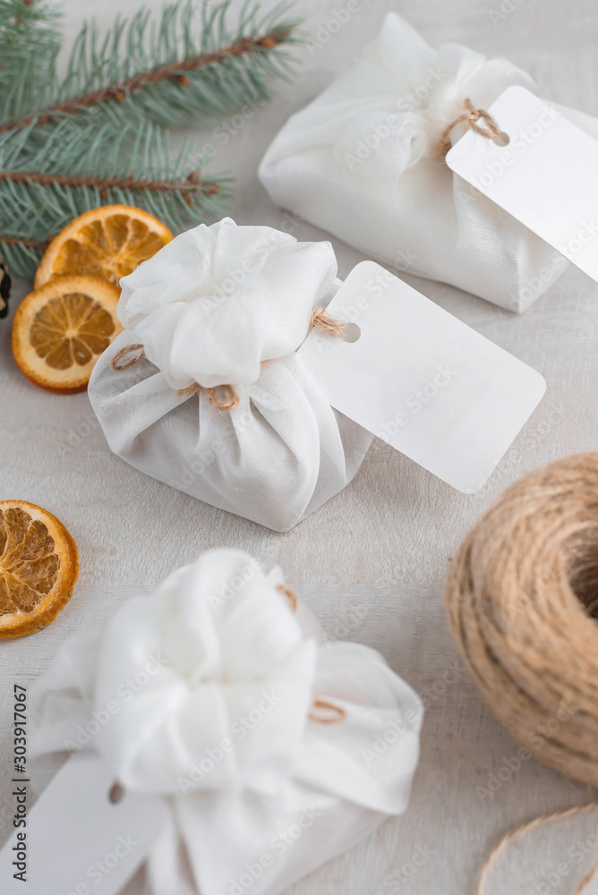 Christmas presents wrapped with white furoshiki fabric, labels and dried orange slices. Eco friendly gift.