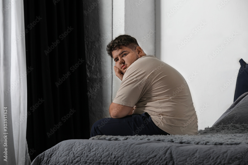 Depressed overweight man on bed at home Depressed overweight man on bed at home