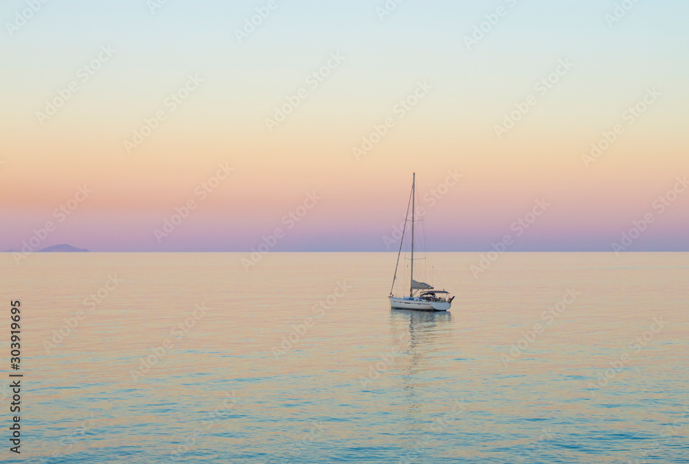 Small white sailboat in Aegean sea by Greek island of Santorini in calm summer evening after sunset.