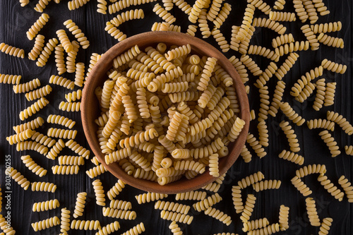 Top view of fusilli pasta in bowl and scattered on black wooden table