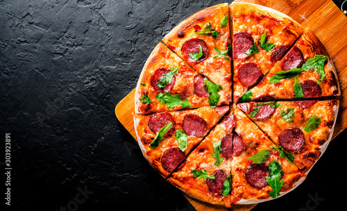 Pepperoni Pizza with Mozzarella cheese, salami, Tomato sauce, pepper, Spices and Fresh arugula. Italian pizza on Dark grey black slate background