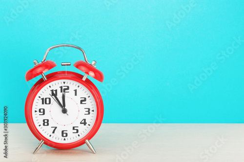 Konstfotografi Red retro alarm clock with five minutes to twelve o'clock, on wooden table on a blue background