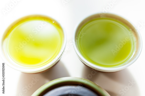 Closeup of small two cups filled with Japanese vibrant green yellow sencha fukamushi or genmaicha tea color for breakfast or ceremony photo