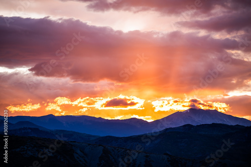Orange purple cloudy sunset sun rays in Aspen, Colorado with rocky mountains peak and vibrant color of clouds at twilight with mountain ridge dark silhouette photo