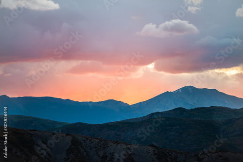 Fototapeta Naklejka Na Ścianę i Meble -  Orange red soft light cloudy sunset sun rays in Aspen, Colorado with rocky mountains peak and vibrant color of clouds at twilight with mountain ridge silhouette