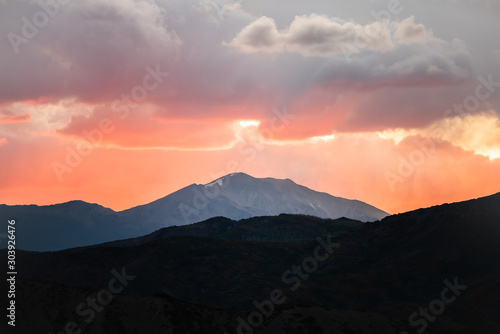 Orange red soft light glow sunset sun rays in Aspen, Colorado with rocky mountains peak and vibrant color of clouds at twilight with mountain ridge silhouette © Kristina Blokhin