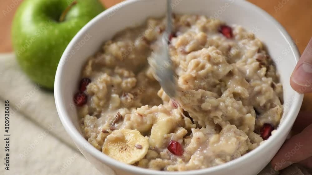 Healthy eating, oatmeal porridge bowl. Person mixing oatmeal with fruits and taking a spoonful of porridge. Closeup view Healthy eating, oatmeal porridge bowl. Person mixing oatmeal with fruits and taking a spoonful of porridge. Closeup view