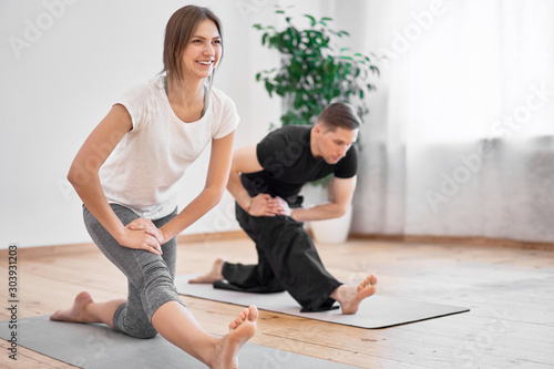 Man and woman doing yoga sitting on gray rug against background of window in room during day