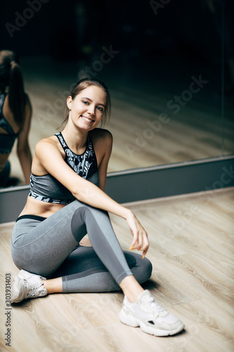 Sportswoman sitting on wooden floor against background of mirror