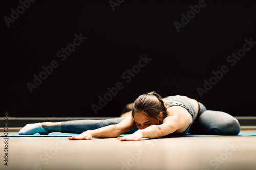 Athletic woman stretching lying on rug in sports hall