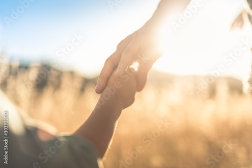 Fényképezés Mother little child holding hands walking in a grass field at sunset