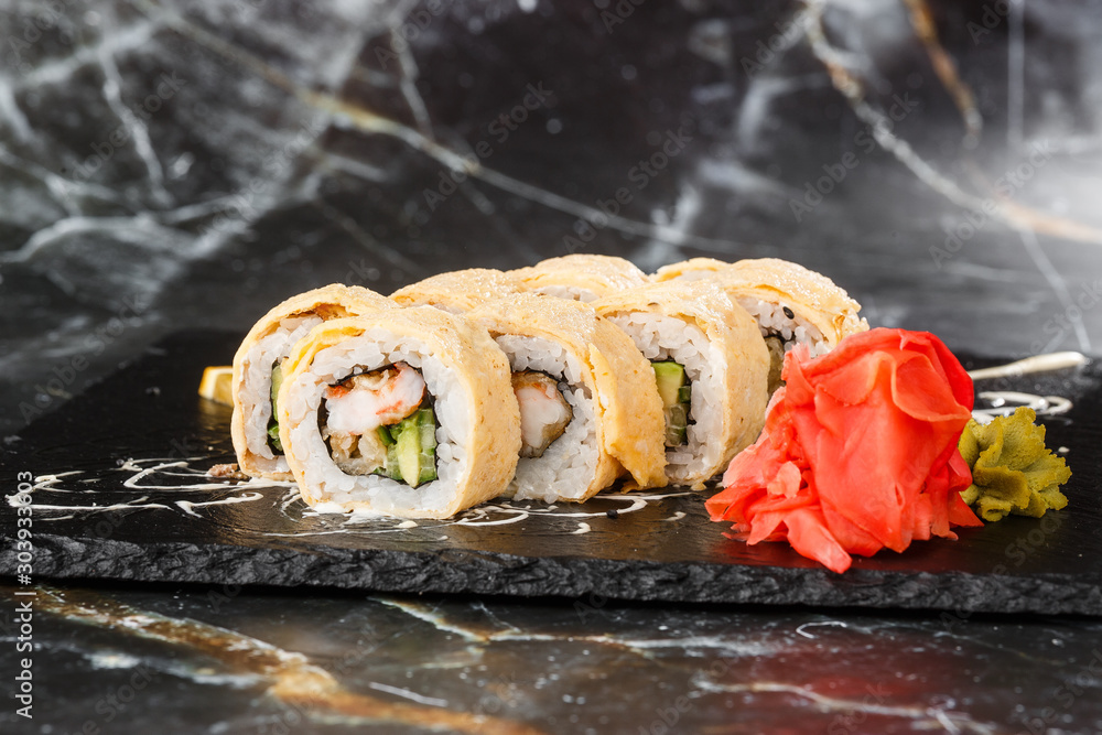 Sushi Rolls with avocado, eel, cucumber and cream cheese inside on black slate isolated on black marble background. California rolls covered on omelet Sushi menu. Horizontal photo.