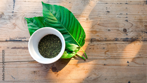 Fotografie powder in white bowl on kratom leaf (Mitragyna speciosa) Mitragynine on wooden ,