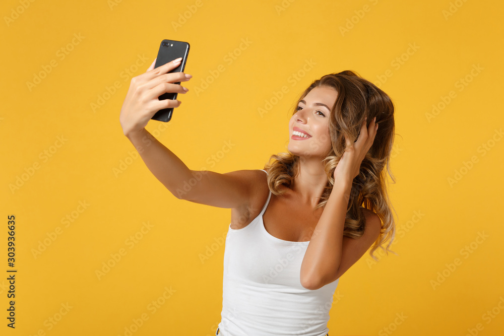 Smiling young woman girl in light casual clothes posing isolated on yellow orange background. People lifestyle concept. Mock up copy space. Doing selfie shot on mobile phone, putting hand on head. Smiling young woman girl in light casual clothes posing isolated on yellow orange background. People lifestyle concept. Mock up copy space. Doing selfie shot on mobile phone, putting hand on head.