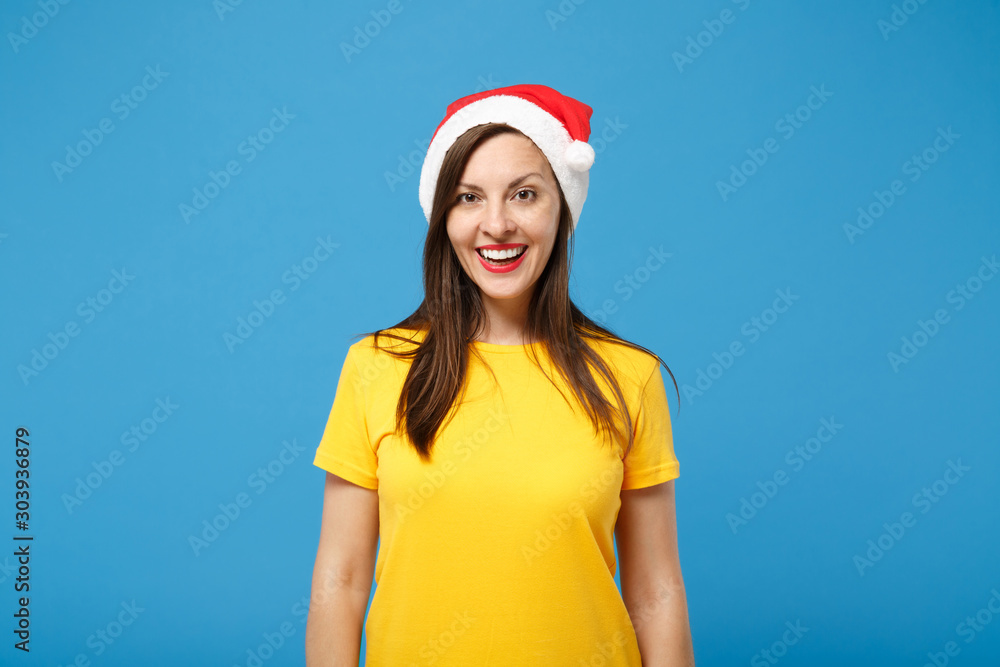 Cheerful young brunette woman Santa girl in yellow t-shirt Christmas hat posing isolated on bright blue background. Happy New Year 2020 celebration holiday concept. Mock up copy space. Looking camera. Cheerful young brunette woman Santa girl in yellow t-shirt Christmas hat posing isolated on bright blue background. Happy New Year 2020 celebration holiday concept. Mock up copy space. Looking camera.