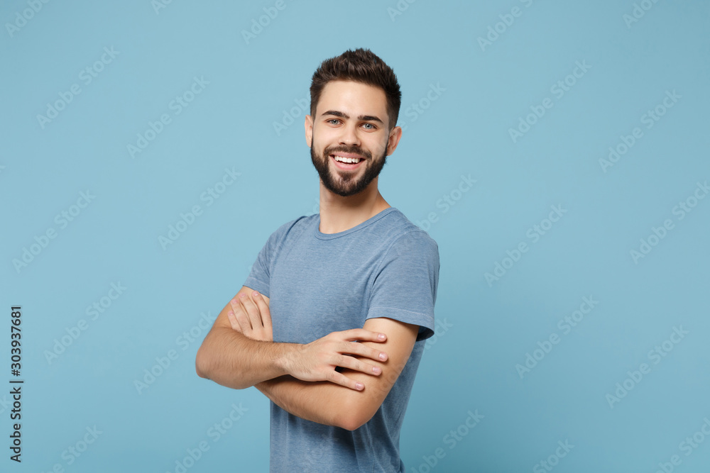 Young smiling cheerful handsome man in casual clothes posing isolated on blue wall background, studio portrait. People sincere emotions lifestyle concept. Mock up copy space. Holding hands crossed. Young smiling cheerful handsome man in casual clothes posing isolated on blue wall background, studio portrait. People sincere emotions lifestyle concept. Mock up copy space. Holding hands crossed.