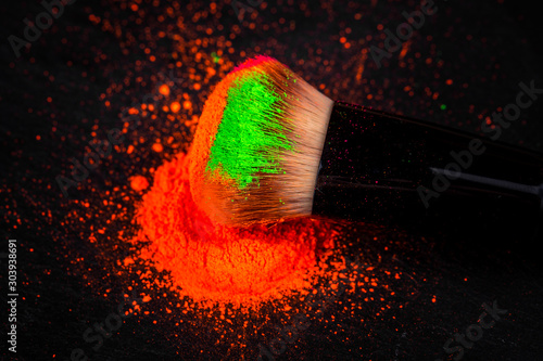 Cheek brush with neon cosmetic powder colorful pile on black background