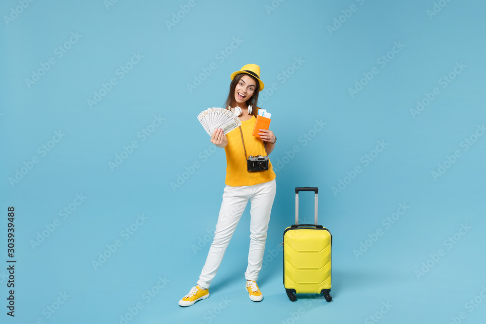 Traveler tourist woman in yellow summer casual clothes hat hold tickets luggage isolated on blue background. Female passenger traveling abroad to travel on weekends getaway. Air flight journey concept Traveler tourist woman in yellow summer casual clothes hat hold tickets luggage isolated on blue background. Female passenger traveling abroad to travel on weekends getaway. Air flight journey concept
