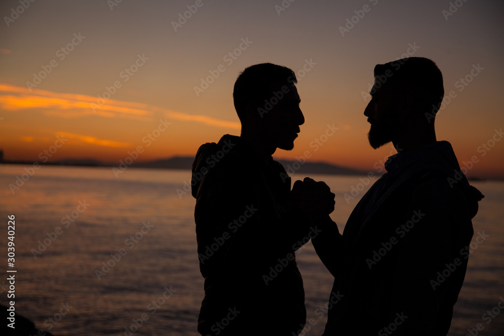 The gay couple jumping on the seaside on the sunset background