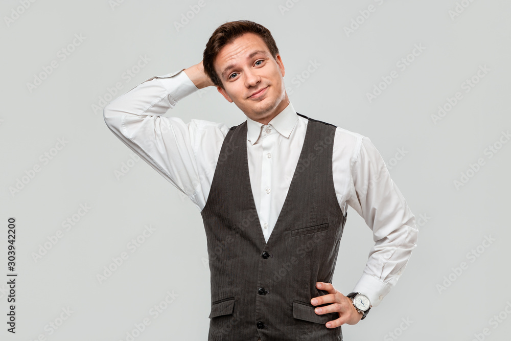 Handsome businessman in a white shirt and grey vest scratching his head over grey background. Handsome businessman in a white shirt and grey vest scratching his head over grey background.