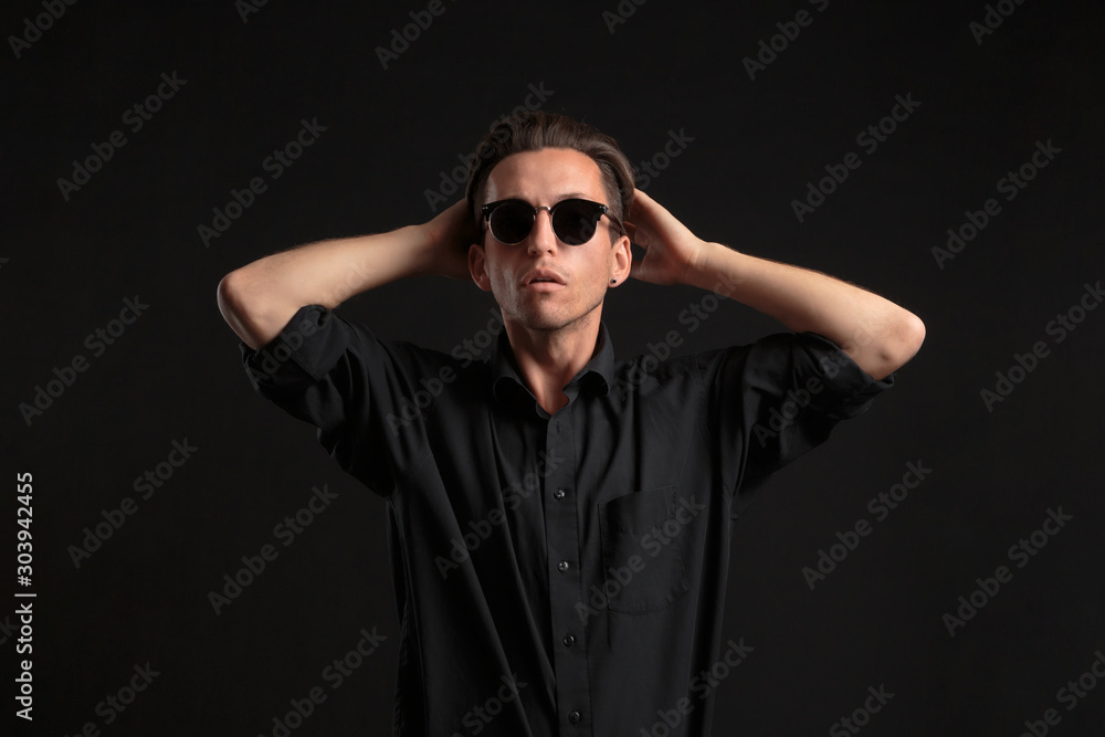 Obraz premium Confident stylish bussinesman in black eyeglasses fixing hair isolated over black background.