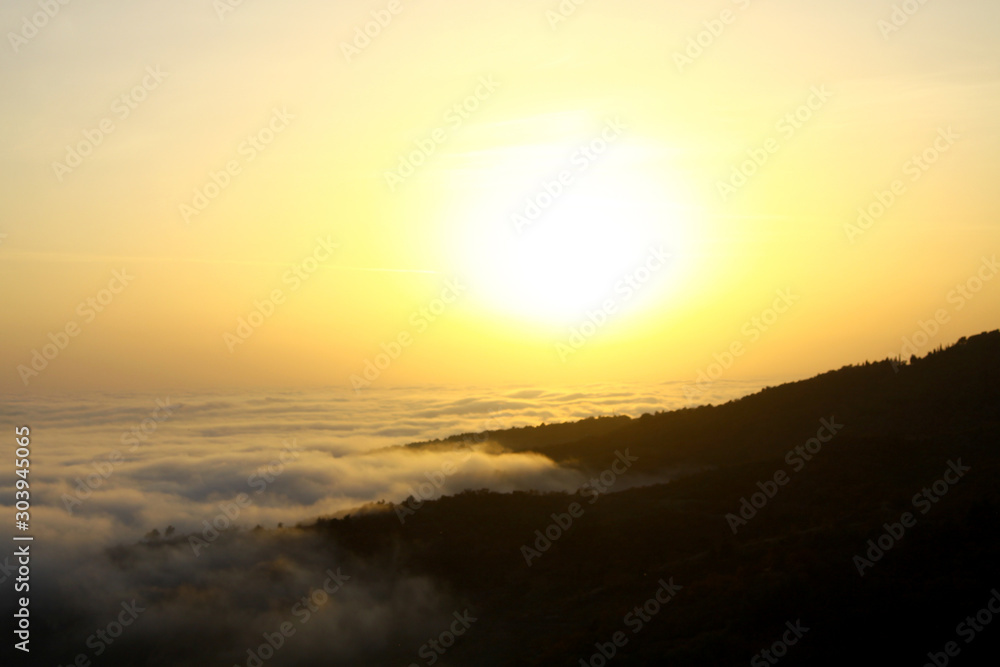 Fog covers the mountains during golden hour and a large ball of sun on the horizon