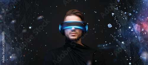 Young man on virtual reality background. Guy using VR helmet. Augmented reality, future technology, game concept. Free space for text. Blue neon light.