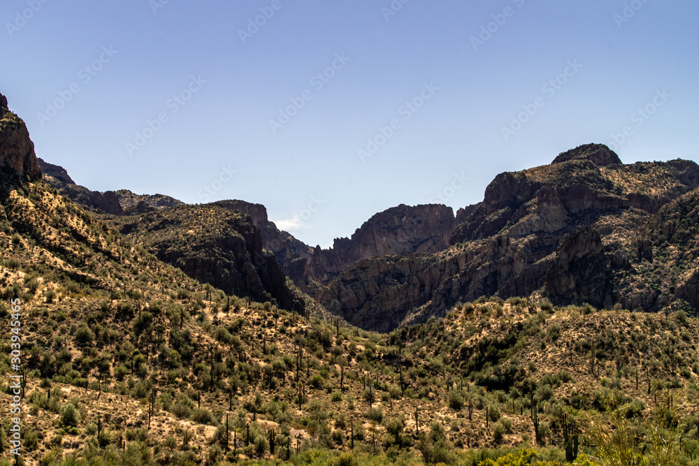 Fototapeta premium Aerial, landscape along the Salt River in Arizona with pink and orange rocks, purple mountains, cool water, blue sky, cactus, green trees and brush on a Fall day