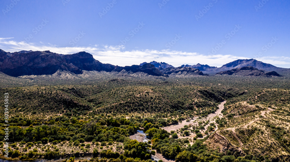 Aerial, landscape along the Salt River in Arizona with pink and orange rocks, purple mountains, cool water, blue sky, cactus, green trees and brush on a Fall day