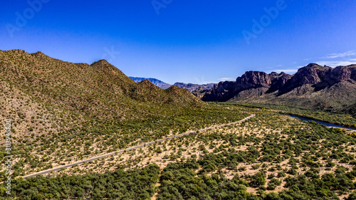 Aerial, landscape along the Salt River in Arizona with pink and orange rocks, purple mountains, cool water, blue sky, cactus, green trees and brush on a Fall day