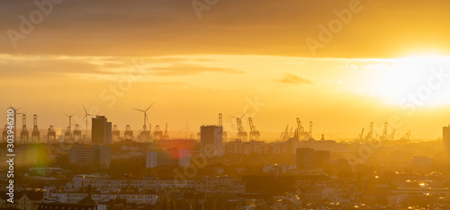 Cranes and wind turbines during sunset in the harbor area of Hamburg, Germany.