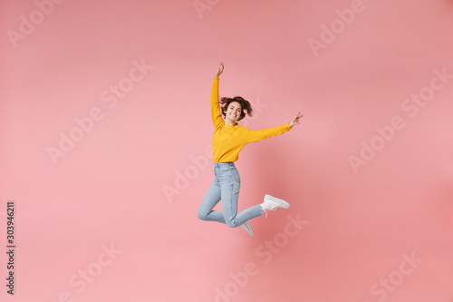 Funny young brunette woman girl in yellow sweater posing isolated on pastel pink background in studio. People lifestyle concept. Mock up copy space. Having fun, fooling around, rising hands, jumping.