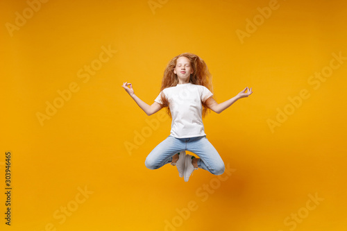 Little ginger kid girl 12-13 years old in white t-shirt isolated on yellow background children portrait. Childhood lifestyle concept. Mock up copy space. Jumping hold hands in yoga gesture meditating.