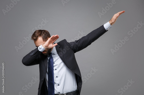 Young bearded business man in classic black suit shirt tie posing isolated on grey background studio portrait. Achievement career wealth business concept. Mock up copy space.Showing DAB dance gesture.