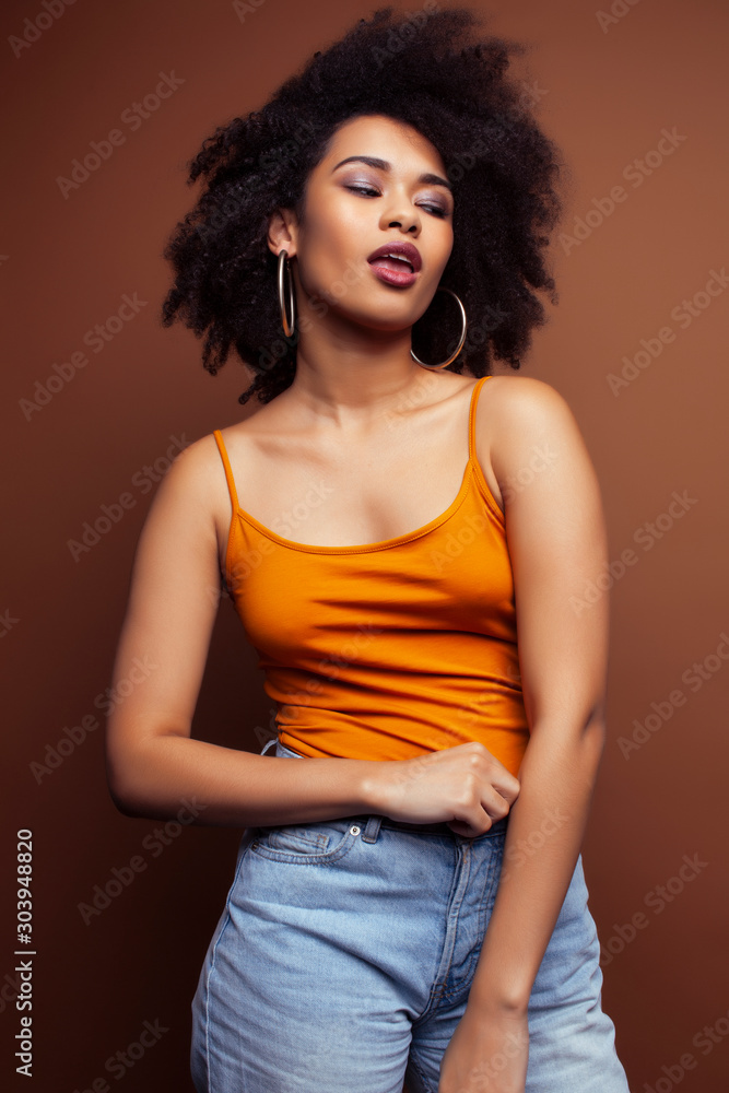 pretty young african american woman with curly hair posing cheerful gesturing on brown background, lifestyle people concept pretty young african american woman with curly hair posing cheerful gesturing on brown background, lifestyle people concept