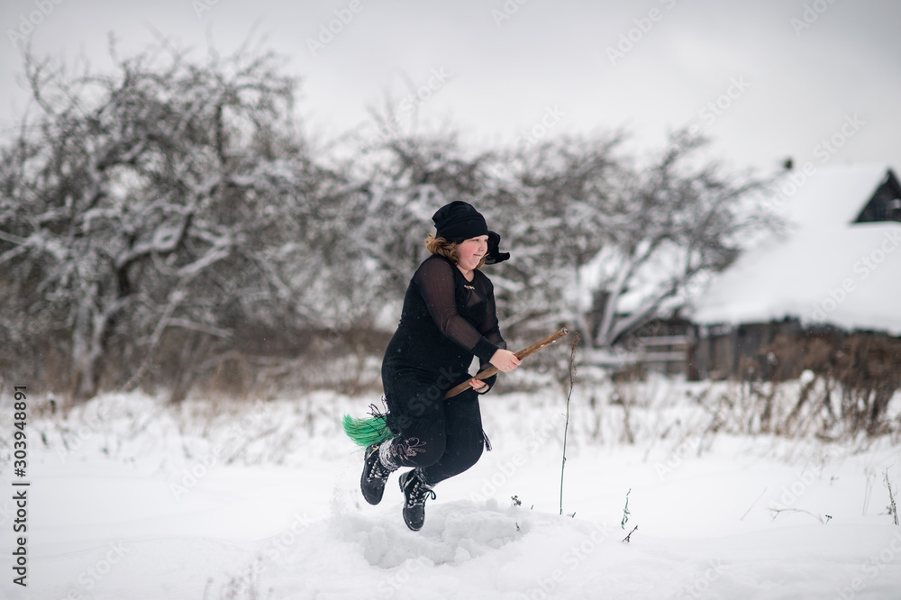Excited girl dressed in with costume starting to gly on her broomstick to coven in snowy winter day in countryside nature.