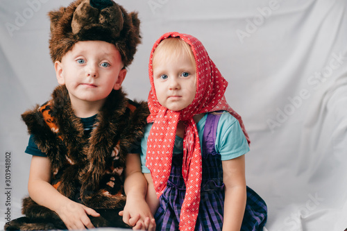 Beautiful couple of lovely children in bear costume and russian cartoon clothes sitting on bed with funny faces. Soft focus portrait of little children in costumes