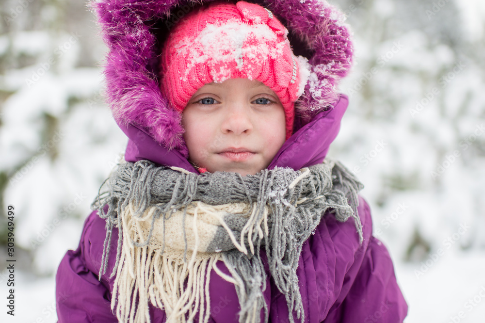 Happy little girl in purple hooded jacket wrapped in scarf with cpositive face looking at camera