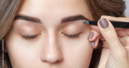 Make-up artist plucks eyebrows with tweezers to a woman. Beautiful thick eyebrows close up. photo