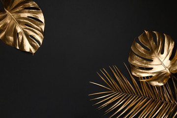 Gold painted tropical leaves on black plain paper background.