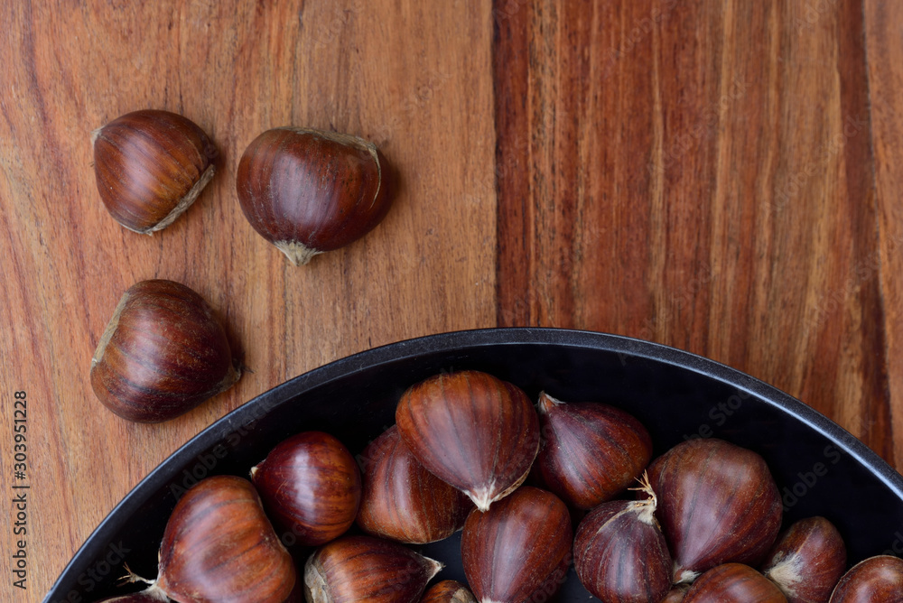 Many brown onesfresh and raw sweet chestnuts in a pan on wooden background Many brown onesfresh and raw sweet chestnuts in a pan on wooden background