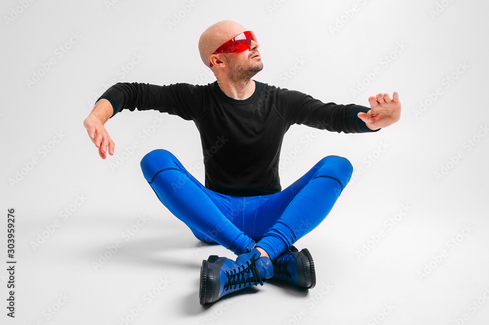 Strange man in stylish clothes and red sunglasses relaxing in studio against white background.